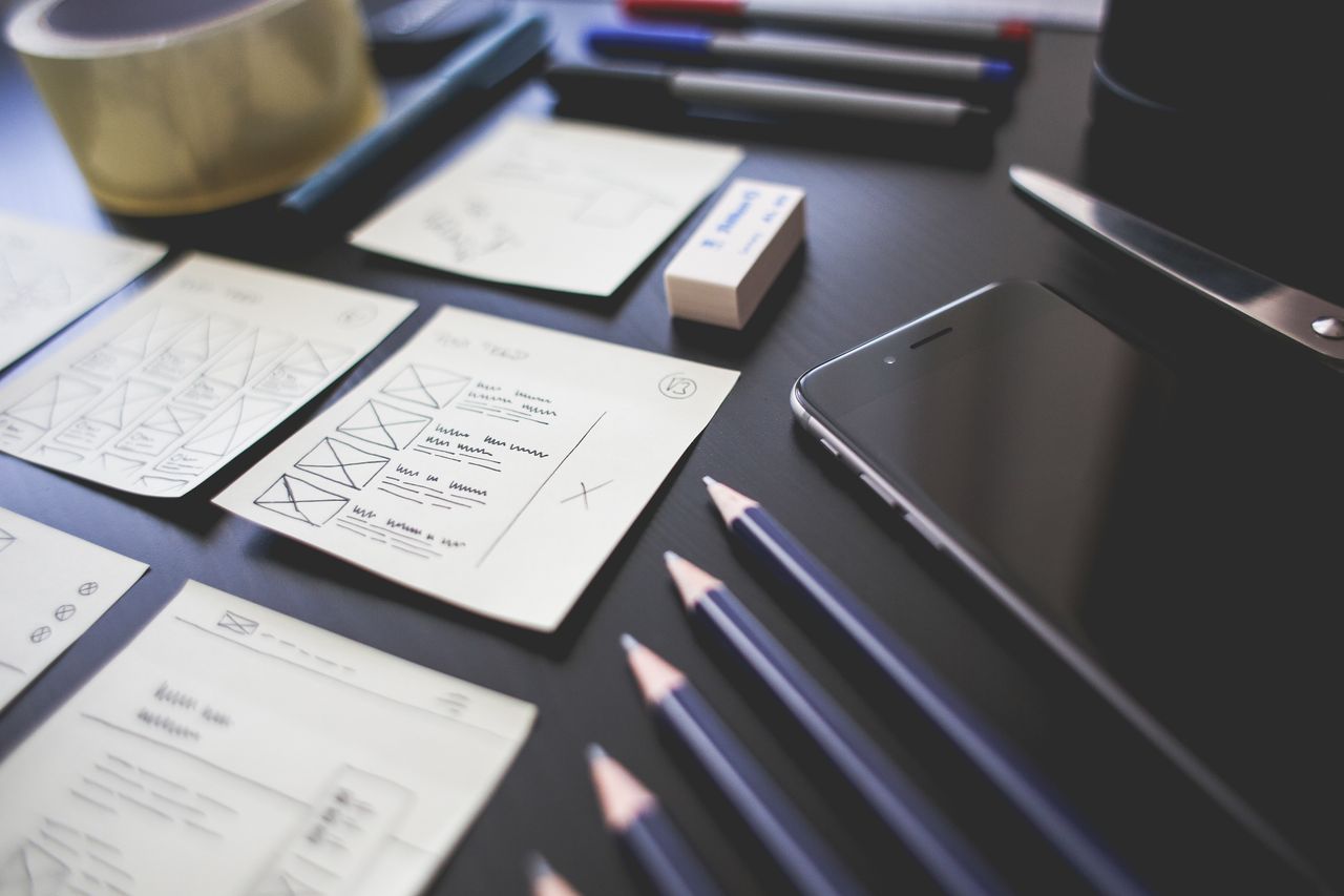 Un espace de travail créatif comprenant des plans de design UI, des crayons, un smartphone et d'autres outils de bureau.